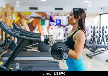 Una donna sta sollevando pesi in una palestra usando un barbell. Foto Stock
