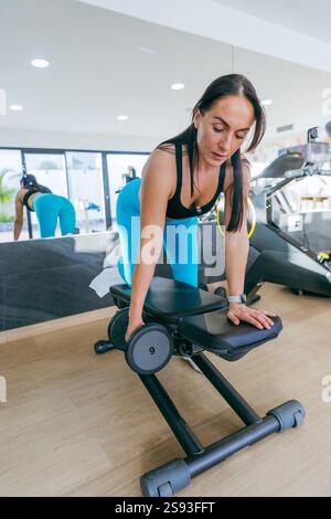 Una donna sta sollevando pesi su una panchina. La panchina ha un numero 9. La donna indossa una canotta nera e pantaloni blu Foto Stock