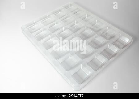 Uno stampo per termoformatura quadrato trasparente industriale realizzato in plastica come soluzione di imballaggio per prodotti industriali. Cubi in lamina su sfondo bianco. Foto Stock