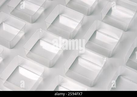 Uno stampo per termoformatura quadrato trasparente industriale realizzato in plastica come soluzione di imballaggio per prodotti industriali. Cubi in lamina su sfondo bianco. Foto Stock