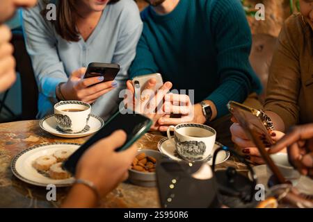 Primo piano di amici che usano smartphone e si gusta un caffè in un accogliente bar. Mette in evidenza la tecnologia moderna, lo stile di vita digitale e l'interazione sociale con Foto Stock