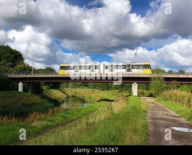 Tram bianco e giallo Metro Link che attraversa il fiume Mersey a South Manchester Foto Stock