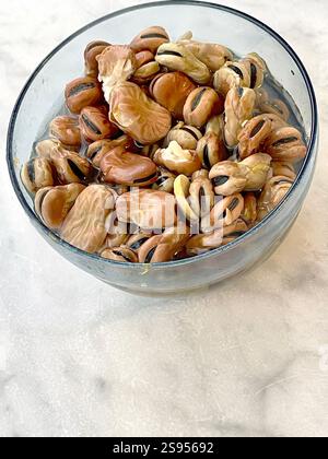 Fagioli immersi in acqua in una ciotola di vetro su un tavolo di marmo. Cibo e mangiare sano. Alimenti proteici. Foto Stock