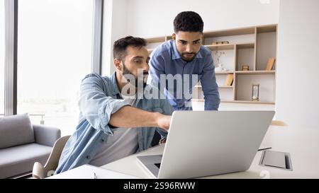 Due colleghi di sesso maschile multietnico che utilizzano un computer portatile sul posto di lavoro Foto Stock