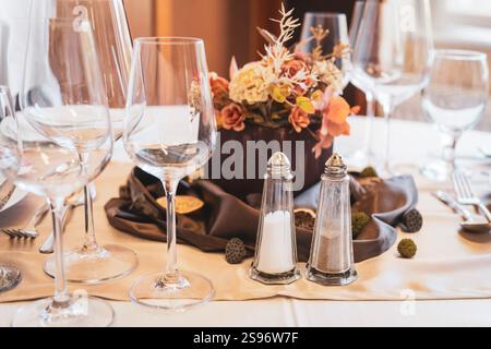 Un tavolo elegantemente allestito con bicchieri da vino multipli, shaker di sale e pepe e un elemento decorativo floreale centrale. Foto Stock