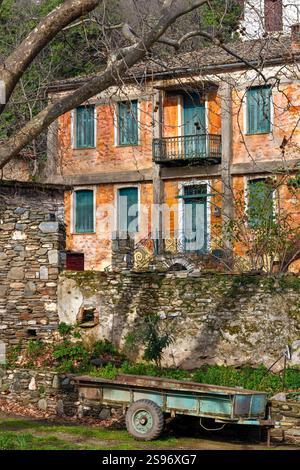 Casa abbandonata a due piani con facciata arancione intemprata, persiane turchesi e un carro rustico nel villaggio di Metaksohori, in Grecia. Foto Stock