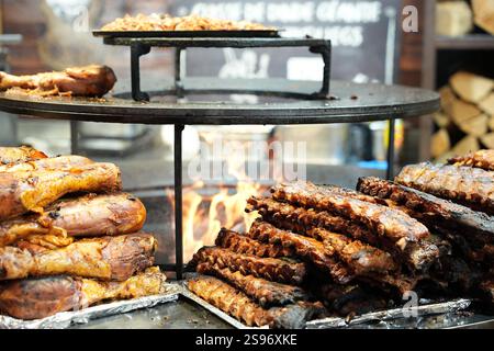 Un primo piano di costolette grigliate e carne arrosto cucinati su una fiamma aperta su un barbecue, creando una scena affumicata e saporita in un mercato di cibo di strada. Foto Stock