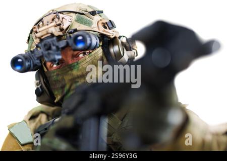 Un soldato delle forze speciali, dotato di equipaggiamento tattico avanzato, tra cui occhiali per la visione notturna, punta la sua arma. Lo sfondo è isolato Foto Stock