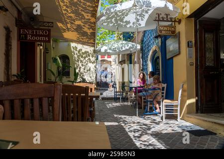 Chania Creta - 15 agosto 2024; famiglia turistica di tre persone che beve bevande fresche all'ombra al tavolo in idilliaci vicoli e strade della città. Foto Stock