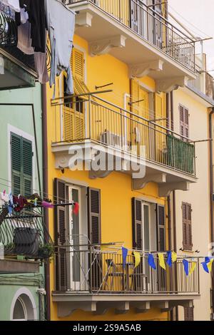 Facciata dell'edificio residenziale rivestito in stucco verde, giallo e beige e asciugatura di vestiti lavati su un armadio sul balcone, Manarola, cinque ter Foto Stock