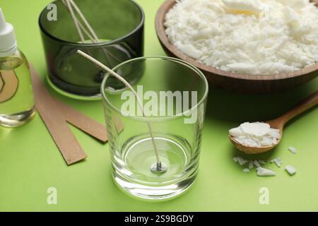 Preparare candele fatte in casa. Cera di soia nel recipiente, vasetti con stabilizzatori, stoppini e olio essenziale su sfondo verde, primo piano Foto Stock