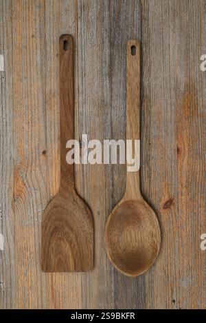 Un paio di utensili in legno, tra cui un cucchiaio e una spatola, esposti su una superficie rustica in legno. Questi utensili da cucina ecologici fatti a mano sono dotati di tecnologia nat Foto Stock
