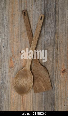 Un paio di utensili in legno, tra cui un cucchiaio e una spatola, esposti su una superficie rustica in legno. Questi utensili da cucina ecologici fatti a mano sono dotati di tecnologia nat Foto Stock