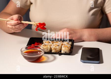 Donna che mangia sushi con le bacchette sul posto di lavoro. Cibo asiatico sano durante la pausa pranzo al lavoro. Sushi in pacchetto da asporto. Gustosi piatti asiatici Foto Stock