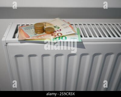 Soldi sulla batteria del radiatore di riscaldamento. Banconote in euro su termostato. Il concetto di aumento dei prezzi del gas e del riscaldamento, prezzi costosi per le bollette Foto Stock