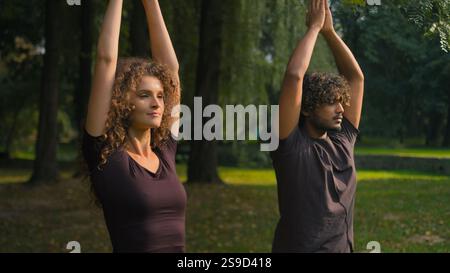 Sport attiva diversità etnica donna uomo allenamento sport insieme fuori classe yoga esercizio di equilibrio con le mani in namaste Arabian sportivo Caucasico Foto Stock