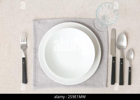 Ambiente minimalista con tovaglia bianca, piatti, vetro e posate sul tavolo Foto Stock