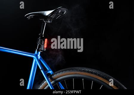 Bici blu ghiaia con illuminazione del lampeggiatore posteriore rosso, sicurezza in bicicletta e design elegante su sfondo scuro con fumo bianco Foto Stock