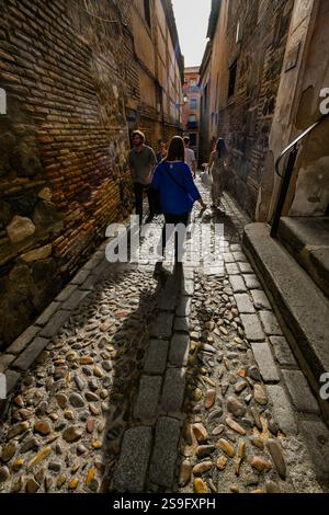 Le figure retroilluminate camminano lungo una stretta strada medievale nella città di Toledo, patrimonio dell'umanità dell'UNESCO, in Spagna, Foto Stock