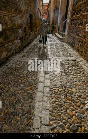 Le figure retroilluminate camminano lungo una stretta strada medievale nella città di Toledo, patrimonio dell'umanità dell'UNESCO, in Spagna, Foto Stock