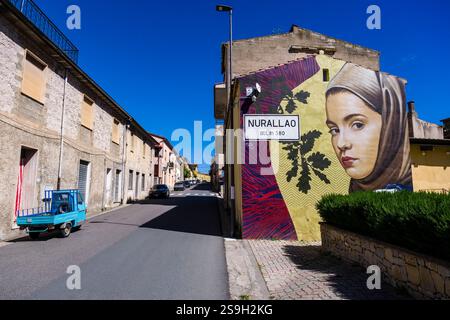 Cartello d'ingresso al paese di Nurallo come parte di un grande graffito con il ritratto di una giovane donna. Foto Stock