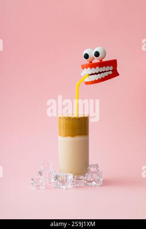 Composizione creativa estiva con finti denti di plastica che bevono caffè ghiacciato su sfondo rosa pastello chiaro. Concetto di caffè estetico. Foto Stock