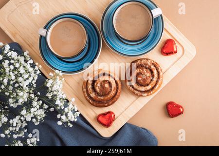 Due tazze di caffè con rotoli di cannella, cioccolatini a forma di cuore e fiori bianchi su un asse di legno. Il giorno di San Valentino. Vista dall'alto, disposizione piatta. Foto Stock