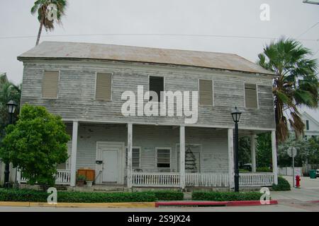 Vecchia casa in legno a due piani con una grande veranda. Cos'è il tetto di latta. Idrante antincendio sulla destra. Palme e cespugli verdi AN Foto Stock