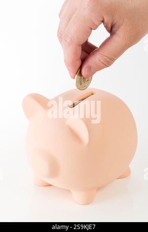 La mano di un uomo che mette monete nel salvadanaio Foto Stock