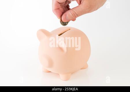 La mano di un uomo che mette monete nel salvadanaio Foto Stock