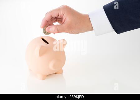 La mano di un uomo che mette monete nel salvadanaio Foto Stock