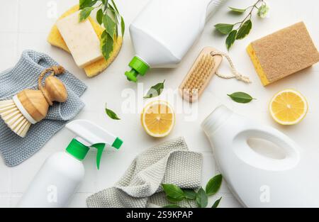 Prodotti per la pulizia naturali, fette di limone, spazzole e spugne disposte su una superficie bianca per una pulizia eco-consapevole Foto Stock