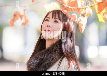 Una donna con i capelli lunghi sulla trentina si trova in una splendida foglie autunnali in una splendida foglie autunnali. Foto Stock