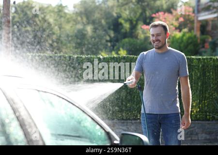 Uomo felice che lava l'auto in un giardino a casa Foto Stock
