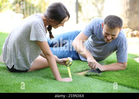 Coppia felice che installa erba artificiale nel giardino di casa Foto Stock