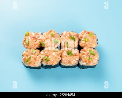 Vista dall'alto del salmone piccante. Fotografia in studio del rotolo di Maki con salmone piccante e cipolla verde decorata. Isolato su sfondo blu chiaro fisso. Posizione piatta Foto Stock