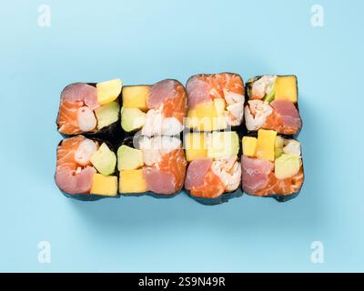 Vista dall'alto del panino hawaiano con mango, avocado, gamberi, salmone e tonno. Fotografia in studio del colorato maki roll hawaiano con gamberi, salmone e tonno. Isolato su sfondo blu chiaro fisso. Foto Stock