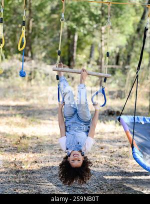 Un bambino sorridente in tuta è appeso al rovescio sulla fune del parco giochi Foto Stock