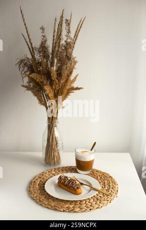 Eclair sul piatto e tovaglietta con caffè e bouquet di fiori secchi Foto Stock