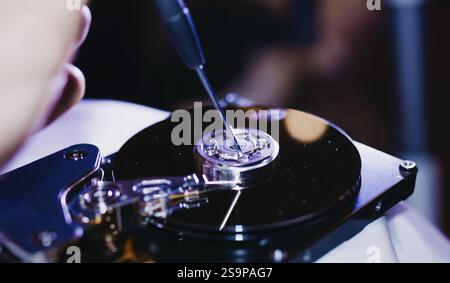 Primo piano di un cacciavite sui componenti di un disco rigido smontato Foto Stock