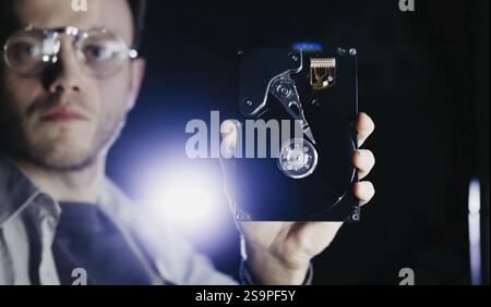 Un uomo che ispeziona un disco rigido, indossa occhiali, con particolare attenzione alla tecnologia e alla precisione Foto Stock