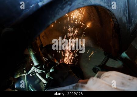 Scintille che volano dal metallo mentre il meccanico lavora sotto il veicolo. Foto Stock