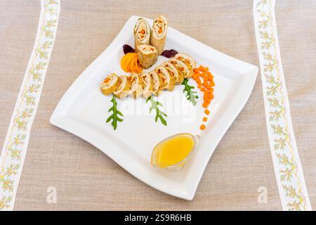 Un piatto di sushi ben organizzato con sushi arrotolato, verdure colorate e una salsa brillante. Questo squisito piatto mette in risalto la freschezza Foto Stock