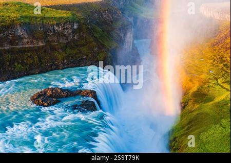 Le cascate d'acqua si innalzano sulla cascata Gullfoss in Islanda, creando una spettacolare nebbia dove appare un arcobaleno. Il paesaggio circostante è perfetto Foto Stock