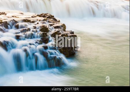 Le cascate d'acqua si innalzano graziosamente su rocce scure e aspre, creando un'atmosfera serena. La luce soffusa del tramonto esalta la bellezza naturale di questo Icelandi Foto Stock