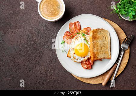 Colazione salutare con uova fritte, pancetta e microgreen su sfondo scuro, spazio copia. Delizioso uovo fritto con pancetta sul pane tostato e colazione Foto Stock