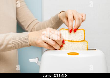 mano di donna che mette il pane nel tostapane. casalinga che frigge il pane in un tostapane, in cucina. donna che fa un brindisi. Foto Stock