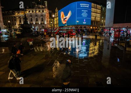 Londra, Regno Unito. 27 gennaio 2025. Il tempo piovoso significava che gli ombrelli erano alzati e, purtroppo, passavano senza nemmeno guardare in alto - Light the Darkness, Holocaust Memorial Day nel 80° anniversario della liberazione di Auschwitz-Birkenau - le Piccadilly Lights, gestite da Ocean Outdoor per conto di Landsec, si uniscono a un momento nazionale che segna il giorno. In un'iniziativa ideata dall'agenzia creativa St Luke's per commemorare i 6 milioni di ebrei uccisi durante l'Olocausto. Crediti: Guy Bell/Alamy Live News Foto Stock