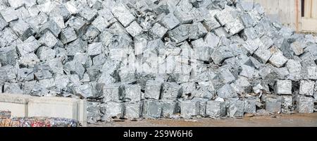 i tratti di cubi in alluminio pressato brillano in una luce brillante, suggerendo operazioni di riciclaggio su larga scala. Le superfici riflettenti evidenziano una spinta industriale Foto Stock