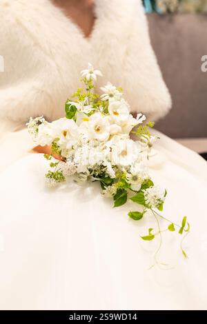La donna indossa un cappotto di pelliccia bianca e tiene in mano un mazzo di fiori bianchi. Il bouquet ha la forma di un fiore e ha uno stelo verde Foto Stock